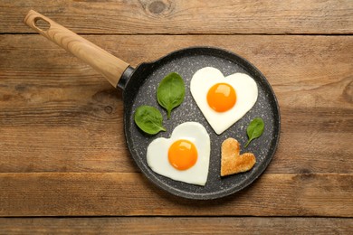 Photo of Heart shaped fried eggs with toast in frying pan on wooden table, top view
