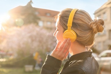 Young woman with headphones listening to music outdoors on sunny day, space for text