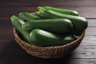 Raw ripe zucchinis in wicker bowl on wooden table