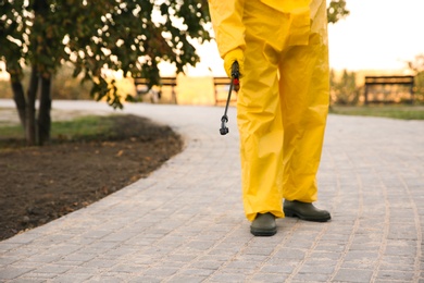 Person in hazmat suit disinfecting pavement in park with sprayer, closeup. Surface treatment during coronavirus pandemic