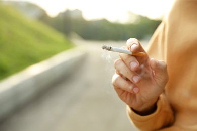 Man with cigarette outdoors, closeup of hand. Space for text