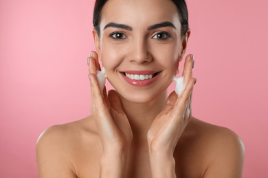 Young woman applying cosmetic product on pink background, closeup. Washing routine