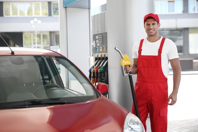 Worker with fuel pump nozzle near car at modern gas station