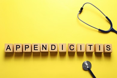 Photo of Word Appendicitis made of wooden cubes and stethoscope on yellow background, flat lay