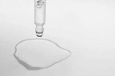 Dripping face serum from pipette on white background, closeup. Space for text
