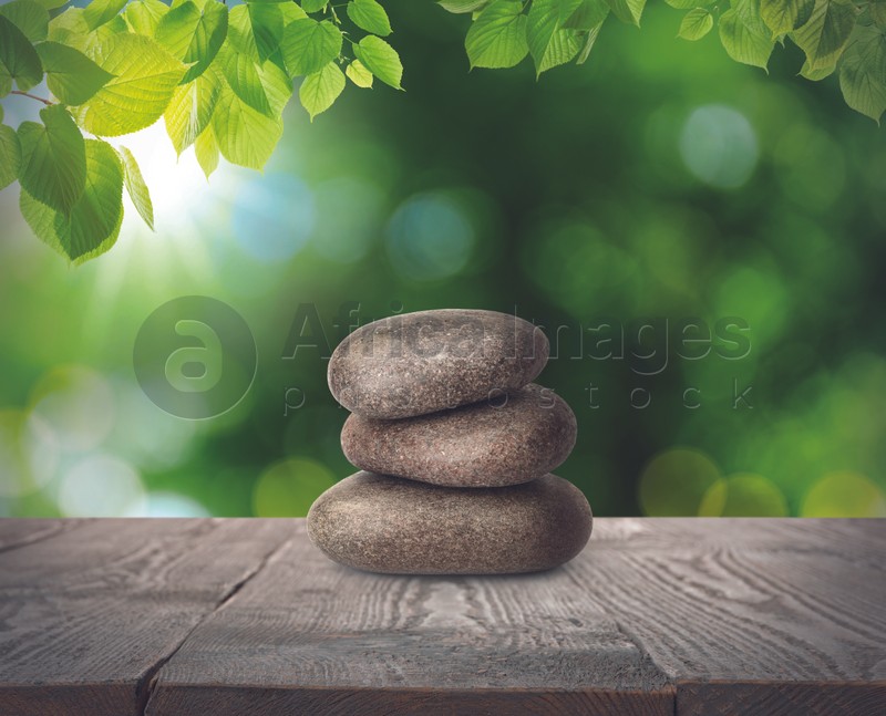 Stacked stones on wooden table under green leaves against blurred background. Zen concept