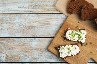 Photo of Bread with cottage cheese and green onion on light blue wooden table, flat lay. Space for text