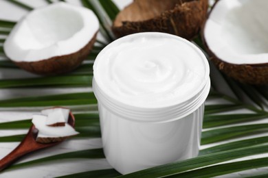 Jar of body cream with palm leaf and coconut on table, closeup