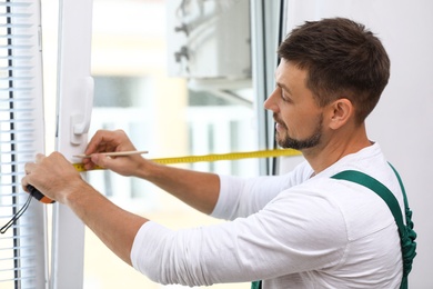 Image of Handyman with tape measure and pencil installing window blinds indoors