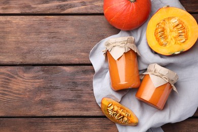 Jars of pumpkin jam and fresh pumpkin on wooden table, flat lay. Space for text