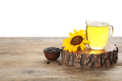 Sunflower, jug of oil and seeds on wooden table against white background, space for text