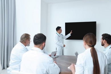 Photo of Team of doctors listening to speaker report near tv screen in meeting room. Medical conference