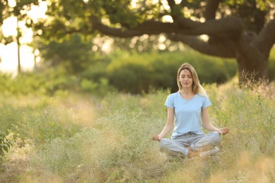 Photo of Young woman meditating on green grass in park, space for text