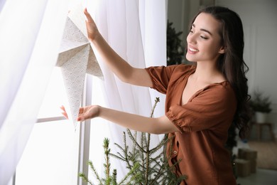 Woman putting decorative star on window at home