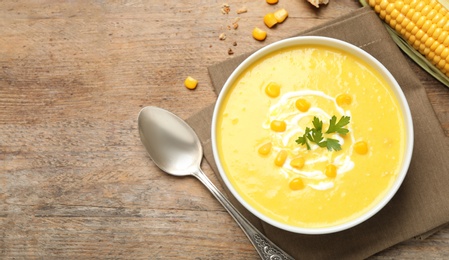 Delicious creamy corn soup served on wooden table, flat lay. Space for text