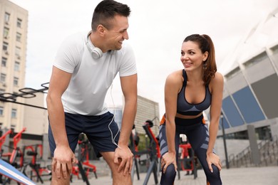 Woman and man in fitness clothes resting near outdoor gym