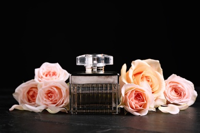 Bottle of perfume and beautiful roses on black table