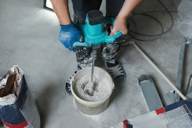 Professional worker mixing plaster in bucket indoors, closeup
