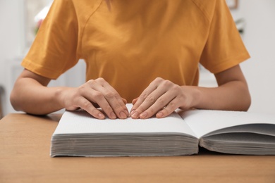 Blind woman reading book written in Braille at table, closeup