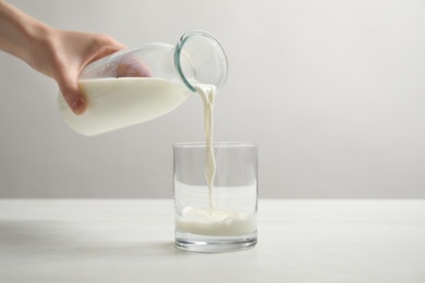 Woman pouring milk into glass at white table, closeup