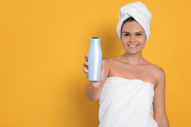Beautiful young woman holding bottle of shampoo on orange background, space for text