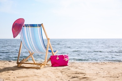 Photo of Lounger, hat and bag on sand near sea, space for text. Beach objects