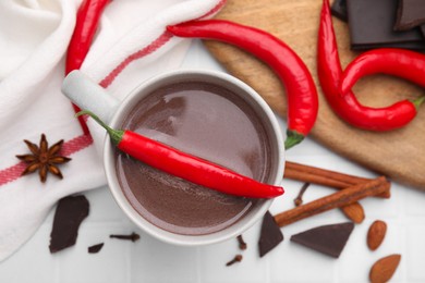Photo of Cup of hot chocolate with chili pepper on white tiled table, flat lay