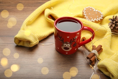 Photo of Cup of hot drink with yellow sweater and Christmas lights on wooden table