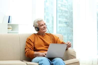 Portrait of mature man with laptop and headphones on sofa indoors