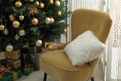 Beautifully decorated Christmas tree and many gift boxes near armchair in room
