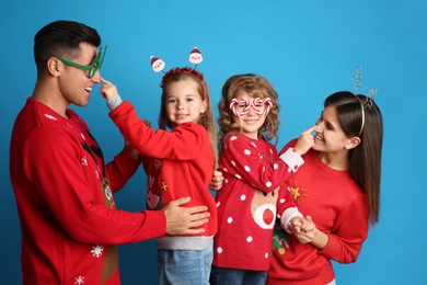 Family in Christmas sweaters and festive accessories having fun on blue background