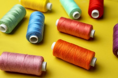 Photo of Different colorful sewing threads on yellow background