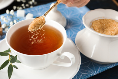 Woman putting brown sugar into tea cup at table, closeup