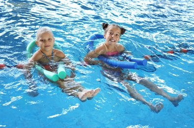 Little girls with swimming noodles in indoor pool