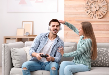 Young woman trying to draw attention of man playing video games at home