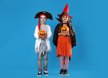 Cute little kids with pumpkin candy buckets wearing Halloween costumes on blue background