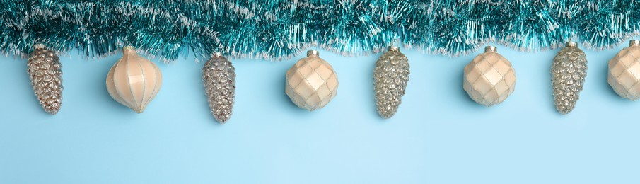 Shiny tinsel and Christmas balls on light blue background, flat lay. Banner design