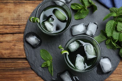 Delicious mint liquor with ice cubes and green leaves on wooden table, flat lay