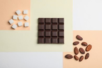 Photo of Delicious dark chocolate bar, refined sugar and cocoa beans on color background, flat lay