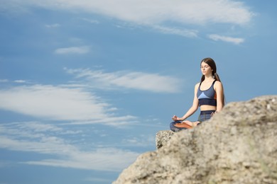 Teenage girl meditating on cliff against blue sky. Space for text