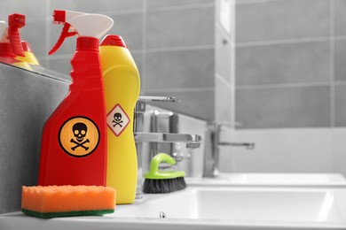 Bottles of toxic household chemicals with warning signs, brush and scouring sponge in bathroom, space for text