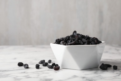 Bowl with raisins on marble table, space for text. Dried fruit as healthy snack