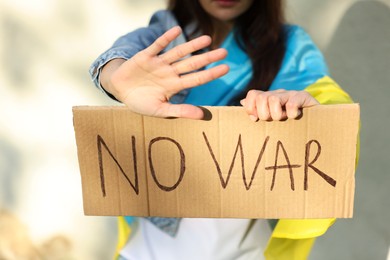 Photo of Young woman holding poster with words No War and showing stop gesture near light wall, closeup
