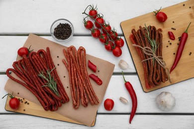 Photo of Delicious kabanosy with rosemary, peppercorn, chilli and tomatoes on white wooden table, flat lay