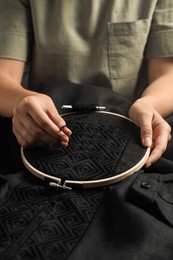 Photo of Woman embroidering black shirt with thread in hoop, closeup. Ukrainian national clothes