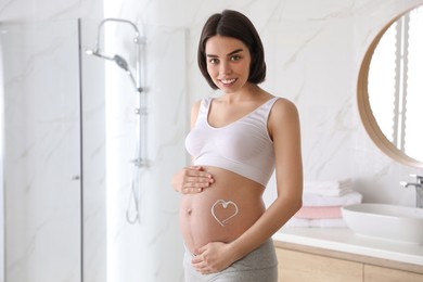 Young pregnant woman with cosmetic product on belly in bathroom