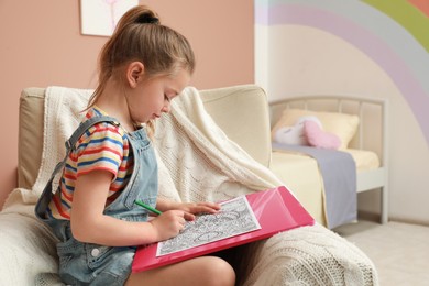 Little girl coloring antistress page in armchair indoors