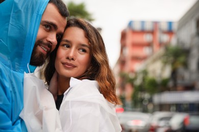 Young couple in raincoats enjoying time together on city street, space for text