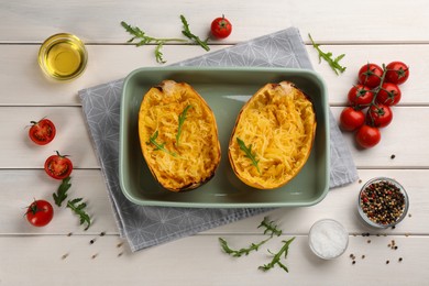 Photo of Halves of cooked spaghetti squash in baking dish and ingredients on white wooden table, flat lay