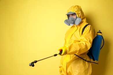 Man wearing protective suit with insecticide sprayer on yellow background, space for text. Pest control